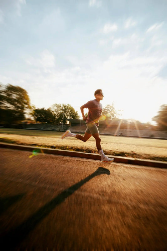 Man running on track during sunrise with lens flare